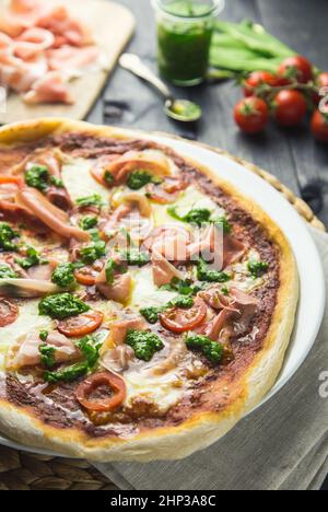 Prosciutto and pesto pizza with cherry tomatoes on a dark wooden background. Stock Photo