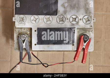 Charging a car starter battery, in a garage, charger clamps connected to positive and negative terminals Stock Photo