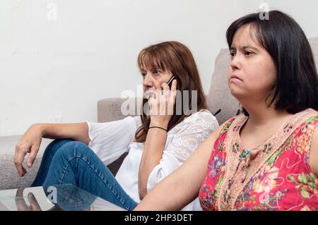 caucasian hispanic latin argentinian mother sitting on the living room floor talking on the phone while her daughter watches television, family and te Stock Photo