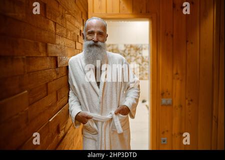 Smiling bearded man in bathrobe relaxing in wooden sauna room at spa resort looking at camera Stock Photo