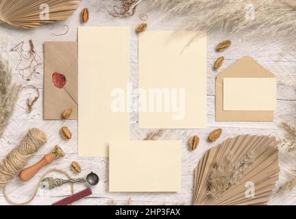 Wedding suite cards and envelope near dried plants, palm leaves and pampas grass top view. Boho scene with blank paper cards flat lay. Wedding set car Stock Photo