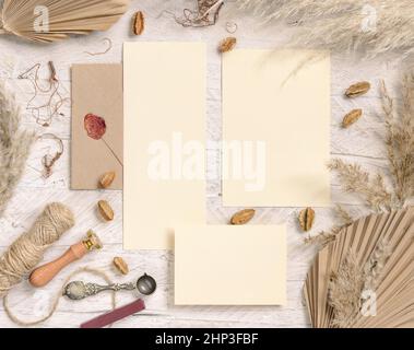 Wedding suite cards and envelope near dried plants, palm leaves and pampas grass top view. Boho scene with blank paper cards flat lay. Wedding set car Stock Photo