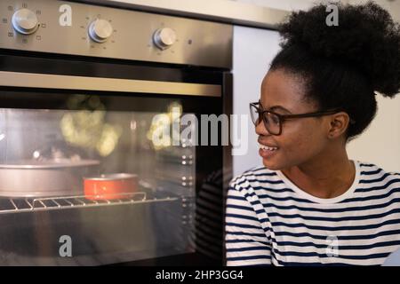 Joyful african woman enjoying process of baking, black female waiting near oven with homemade pastry Stock Photo