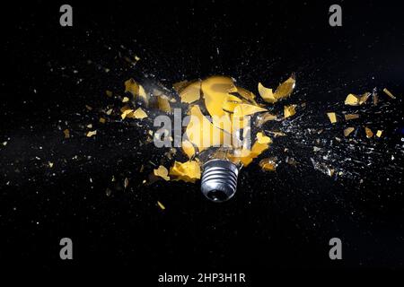high speed photograph of a yellow light bulb exploding on black. Stock Photo