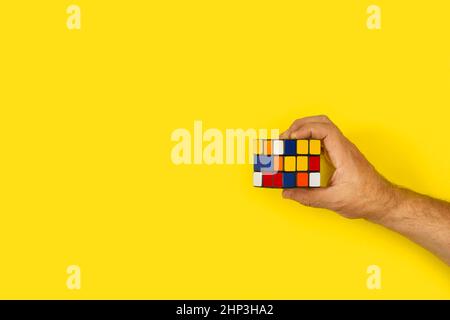 Man hand holing a Rubic cube on a yellow background with copy space Stock Photo