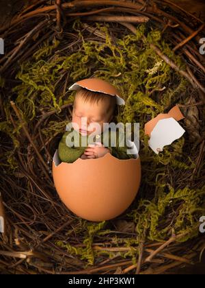 Adorable little newborn baby boy of only 11 days old sleeping in a chicken egg with an eggshell hat Stock Photo