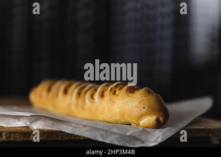baguette bread with a bright crispy crust lies on parchment on a wooden table, dark background, side view Stock Photo