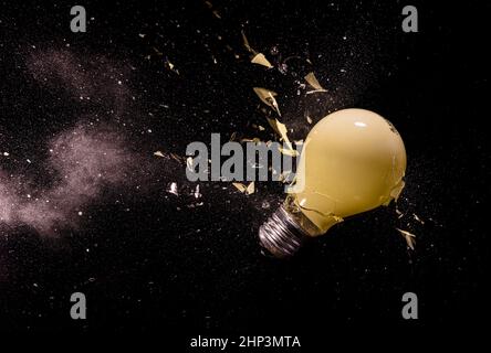 yellow light bulb breaking on black. Stock Photo