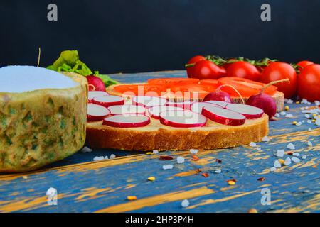 Spread butter on bread with sliced tomatoes and radishes. Fresh snack on natural wooden background. Stock Photo