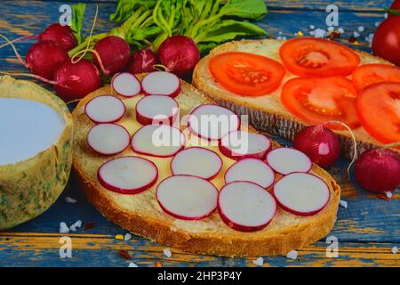 Spread butter on bread with sliced tomatoes and radishes. Fresh snack on natural wooden background. Flat design. Top view. Stock Photo