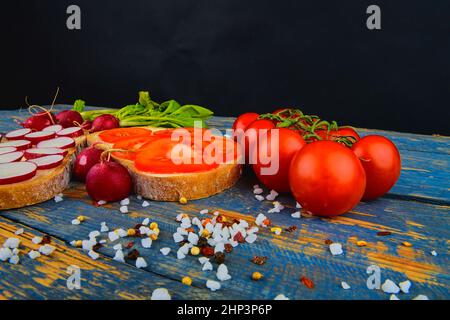 Spread butter on bread with sliced tomatoes and radishes. Fresh snack on natural wooden background. Stock Photo