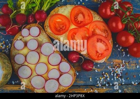 Spread butter on bread with sliced tomatoes and radishes. Fresh snack on natural wooden background. Flat design. Top view. Stock Photo