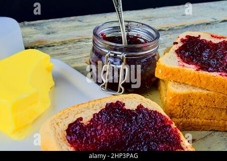 Jam, butter in butter dish and jam spread on toast. Healthy and diet concept. Rural white wooden background. Stock Photo