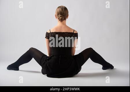 Ballerina sits on the background with her back, legs spread apart. High quality photo Stock Photo