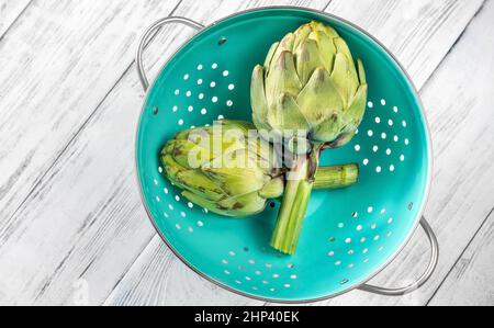 Two uncooked green artichokes in the colander Stock Photo