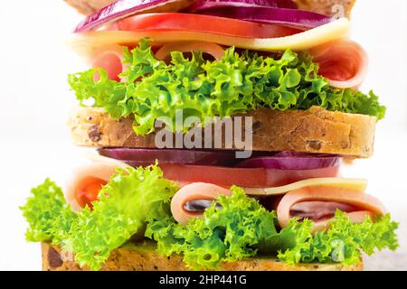 sandwich with ham cheese tomatoes lettuce onions. Macro of multi-layer sandwich with whole grain bread on white background Stock Photo