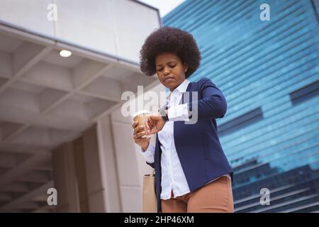 African american mid adult businesswoman checking time while standing with disposable cup in city Stock Photo