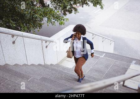 African american mid adult businesswoman talking on phone while rushing steps in city Stock Photo
