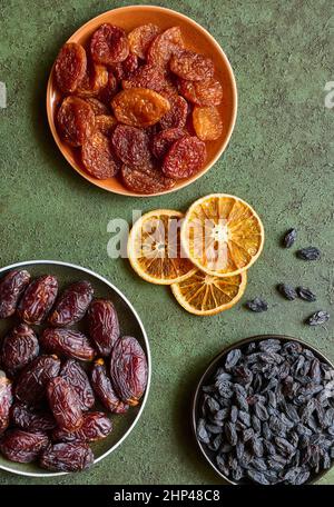 Dried apricots, raisins, dates and slices of dried orange, flat lay on a green background Stock Photo
