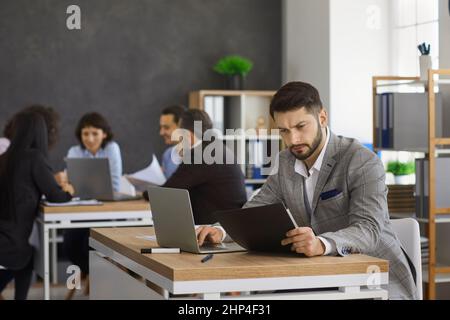 Busy man sits at a table and checks documents while working in a modern bright office. Stock Photo
