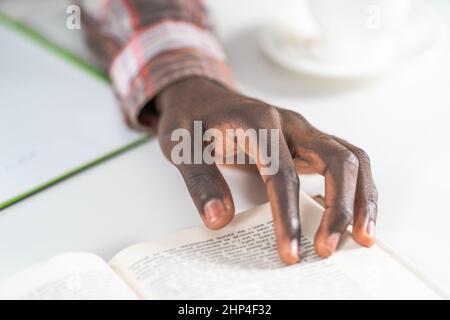 Close up on young male hand of african american man reading book making notes. Student preparing to the lecture at library reading books and making notes. Adduction concept.  Stock Photo
