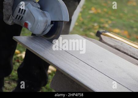 worker cutting a tile using an angle grinder at construction site Stock Photo