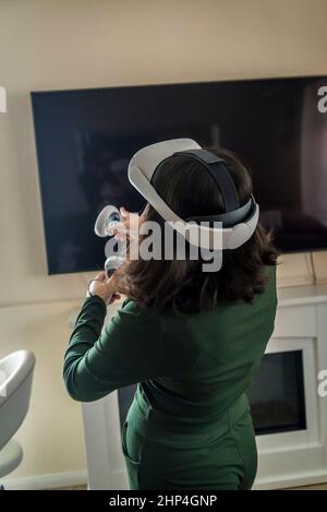 Girl with VR headset and two controllers playing with friends in virtual reality, London, UK Stock Photo