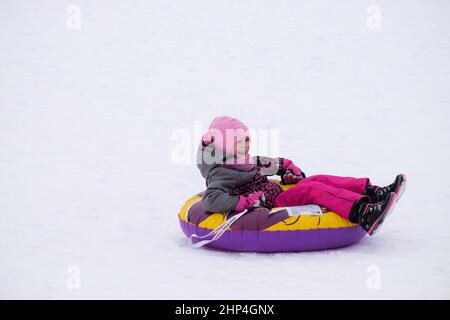 Cute kids sledding and having fun in the snow. A small girl slides quickly on a sled. Screaming with joy and smile. Stock Photo