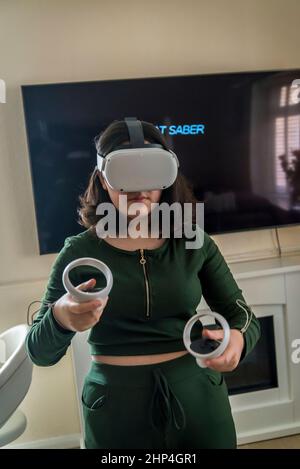 Girl with VR headset and two controllers playing with friends in virtual reality, London, UK Stock Photo