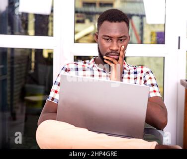 Serious adult businessman sitting on a chair using a laptop with hand on chin. Stock Photo