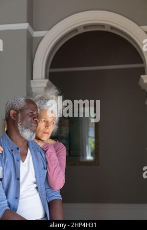 Thoughtful senior diverse couple at home together, embracing and looking away Stock Photo