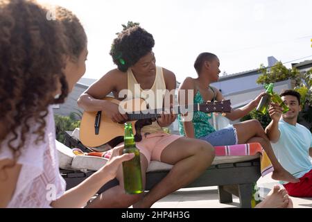 Happy multiracial friends enjoying sunny day at poolside while man playing guitar Stock Photo