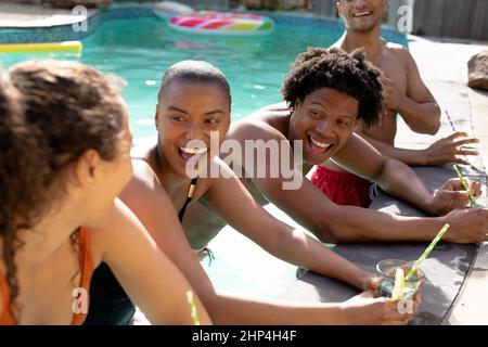 Cheerful multiracial friends laughing while enjoying sunny day in swimming pool Stock Photo