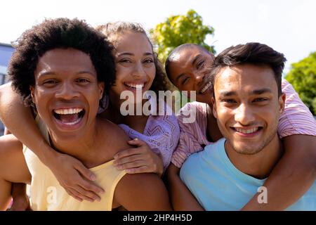 Portrait of smiling multiracial men giving piggyback rides to women on sunny day Stock Photo