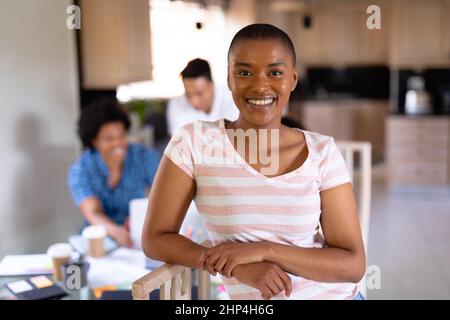 Portrait of smiling young biracial businesswoman standing against colleagues at home office Stock Photo