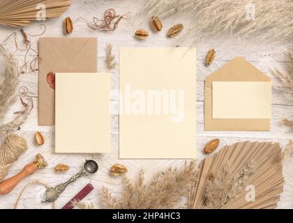 Wedding suite cards and envelopes near dried plants, palm leaves and pampas grass top view. Boho scene with blank paper cards flat lay. Wedding set ca Stock Photo
