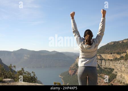 Back view portrait of a happy trekker raising arms in nature celebrating success Stock Photo