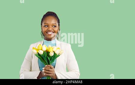 Portrait of beautiful young woman with bouquet of fresh spring tulips on light green background.
