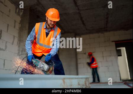 Builder worker in uniform with wheel grinder machine cutting metal parts at construction site Stock Photo