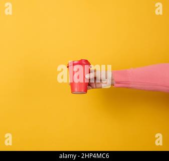 hand holds paper cardboard red cup for coffee, yellow background. Eco ...