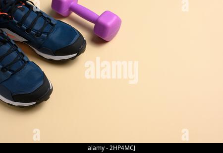 pair of blue sneakers and purple dumbbells on a beige background, sports. Copy space Stock Photo