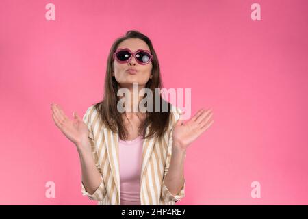 Suffering of headache or migraine young woman in sleeveless pink t-shirt holding her head with eyes shut isolated on pink background. Stressed employee woman in stripe suit. With copy space.  Stock Photo