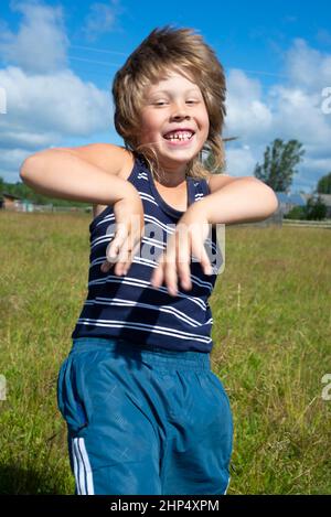 The boy dances in a meadow in nature. Emotions of joy. Laugh. Carefree childhood. Stock Photo
