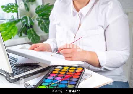 Online learning, hobby classes concept. Girl woman faceless close-up angle learns to paint pictures, draw. Hands with a painting, paints and a brush, Stock Photo