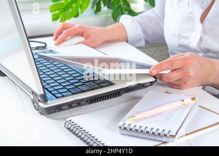 Works with multiple gadget devices at the same time. Woman or girl faceless close-up angle uses smartphone, tablet, laptop. Office work, multitasking Stock Photo