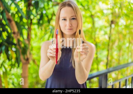 Woman holds eco natural bamboo toothbrush and in other hand plastic toothbrush. rustic background. sustainable lifestyle concept. zero waste. choice Stock Photo