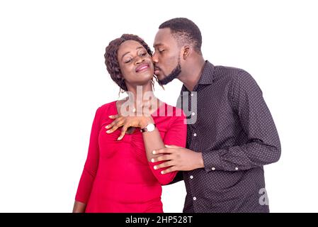a handsome young african man standing on a white background giving a kiss to his girlfriend smiling. Stock Photo