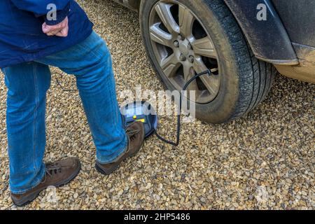 Woman inflating a tyre on a SUV using a portable air compressor run from the car's battery. Stock Photo