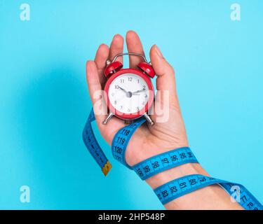 Alarm clock red color in woman hand on bright blue background