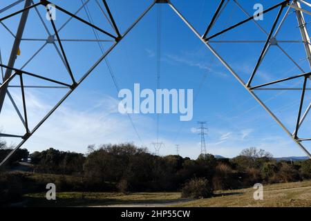 closeup under view of towering steel pylon supporting electric power cables on blue sky Stock Photo